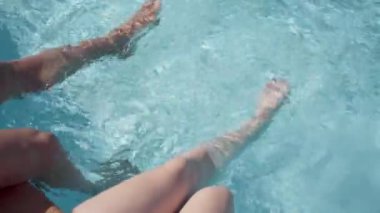 Otelde dinlenirken, havuzda turkuaz suyu olan bir kızla bir adamın bacaklarının hareketi.