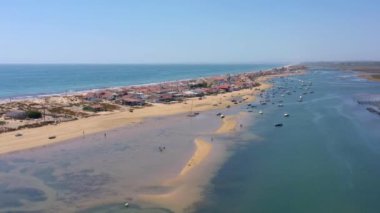 Okyanus kıyısının ve plajın havadan görünüşü. Sudaki tekneler ve kumsalda dinlenen turistler bir İHA 'dan görüldüğü gibi. Praia de Faro Algarve Portekiz. Yüksek kalite 4k görüntü