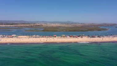 Okyanus kıyısının ve plajın havadan görünüşü. Sudaki tekneler ve kumsalda dinlenen turistler bir İHA 'dan görüldüğü gibi. Praia de Faro Algarve Portekiz. Yüksek kalite 4k görüntü