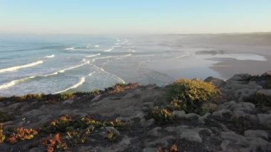 Portekiz 'de güneş doğarken Praia do Malhao sahilinin sisli ve sisli görüntüsü. Gündoğumunda uçurumun üzerinde uçmak