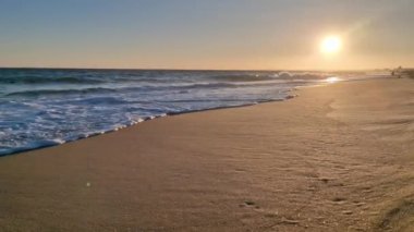 Kumsalda altın gün batımı köpüklü dalgalar kumsalda yuvarlanıyor düşük güneş ışığı altında. Yavaş çekim fotoğrafçılık. Hiç kimse. Rahatlama ve tatil kavramı
