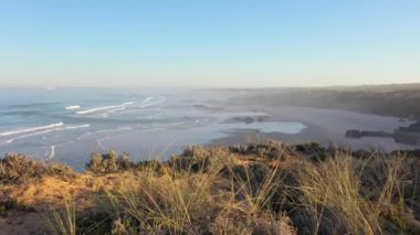 Portekiz 'de güneş doğarken Praia do Malhao sahilinin sisli ve sisli görüntüsü. Kuru otlar ve kayalık uçurumlarla dolu bir kıyıda uçuyor..