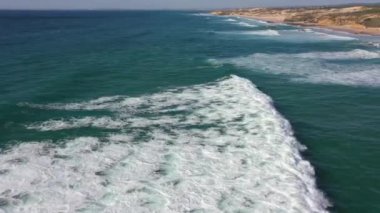 Portekiz 'de güneş doğarken Praia do Malhao sahilinin sisli ve sisli görüntüsü. Yüksek kalite 4K görüntü. İnsansız hava aracı dalgayı yakalıyor..