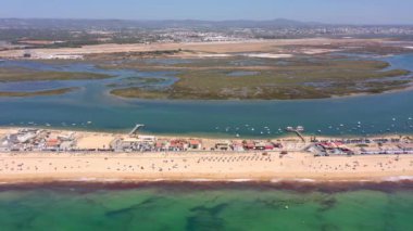 Okyanus kıyısının ve plajın havadan görünüşü. Sudaki tekneler ve kumsalda dinlenen turistler bir İHA 'dan görüldüğü gibi. Praia de Faro Algarve Portekiz. Yüksek kalite 4k görüntü