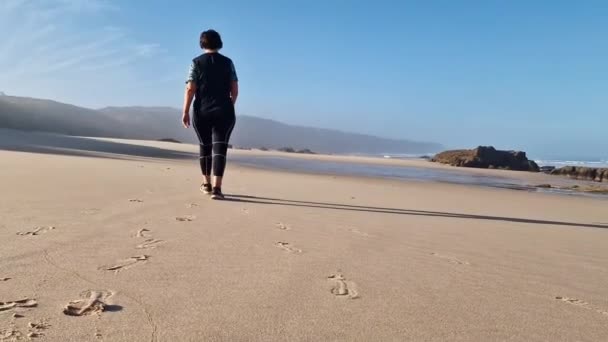 穿着运动服的中年妇女穿着运动服在靠近大海的野生海滩上散步 健康的生活方式概念 优质Fullhd影片 — 图库视频影像