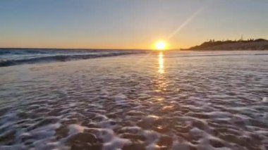 Kumsalda altın gün batımı köpüklü dalgalar kumsalda yuvarlanıyor düşük güneş ışığı altında. Yavaş çekim fotoğrafçılık. Hiç kimse. Rahatlama ve tatil kavramı