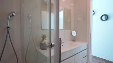 Minimalist beyaz banyo, modern kibir, büyük ayna ve küçük bir bitki ve rulo havlular da dahil olmak üzere zarif bir dekor. Temizlik kavramı ve çağdaş ev tasarımı