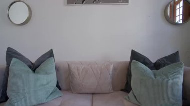 Modern duvar aynaları ve minimalist dekorlarla tamamlanmış, yumuşak desenli yeşil tonlu yumuşak yastıklı şık bej kadife bir kanepe. Rahat ve çağdaş oturma odası tasarımı