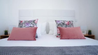 Yatak başlığı beyaz, yumuşak pembe ve çiçek desenli yastıkları olan modern bir yatak odası ve düzgün yapılmış bir yatakta dokulu gri bir battaniye. Şık ve rahat iç tasarım kavramı