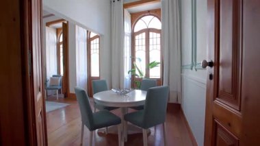 Yuvarlak beyaz masalı zarif yemek alanı, döşeme döşemeleri ve uzun kemerli ahşap çerçeveli ve yemyeşil renkli camlarla çevrili dekoratif gümüş süslemeler. Klasik iç mekan kavramı.