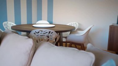 Yuvarlak ahşap masa tarzı beyaz sandalyeler ve ön planda koyu mavi çizgili bej renkli kanepe ile modern yemek alanı minimalist tasarım ekler. Çağdaş ve zarif ev dekorasyonu kavramı