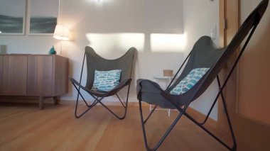 Minimalist yaşam alanı, iki siyah kelebek koltuğu, desenli mavi yastıklar ve ahşap bir büfe. Çağdaş iç zarafet kavramı