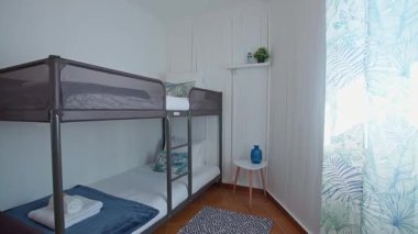 Mavi ve tropikal desenli mavi sehpası olan, rahat, beyaz ahşap bir odada modern ranza. Mavi vazo ile küçük bir yan masa. Pencerenin yanına dekoratif bir dokunuş ekler.