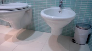Duvara monte edilmiş beyaz seramik tuvalet ve turkuaz mozaik kaplama duvarlara karşı minimalist tasarımı olan modern bir banyo. Estetik ve temiz iç mekan kavramı