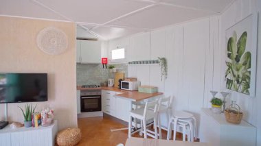 Parlak ve havadar boho tarzı mutfak ve beyaz ahşap duvarlı yaşam alanı, modern aletler ve doğal dekor. Yumuşak pastel tonlar ve kırsal öğeler ev konforu ve şık iç mekan kavramı