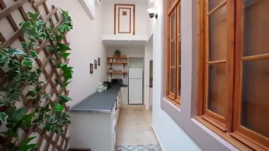 Yüksek tavanlı, beyaz duvarlı, ahşap raflı, koyu tezgahlı, minimalist dekorları, bitkileri ve buzdolabı olan modern mutfağı daraltın. Kompakt ev tasarımı kavramı.