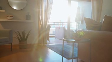 Rahat, modern oturma odası bej bir kanepe dekoratif yastıklar ve metal bir sehpanın üzerinde küçük bir saksı bitkisi. Güneş ışığı cam kapılardan geçer, modern ev konforu kavramı