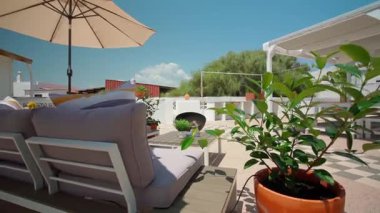 Yumuşak yastıklı kanepe, yeşil bitkiler ve güneş şemsiyeli gökyüzü ve doğal dekor ile açık hava konforu ve doğadan esinlenilmiş tasarım kavramı yaratan açık hava oturma alanının yakın çekimi.