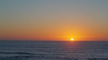Gün batımında okyanusun nefes kesen manzarası, altın güneş ufka batarken, gökyüzünde sıcak bir parıltı yayıyor ve suyun üzerinde canlı turuncu ve mavi renkleri yansıtıyor..