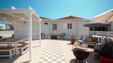 Kareli fayanslı avlusu, şık teras mobilyası ve gür yeşilliği olan büyüleyici beyaz ahşap bir ev. Açık mavi gökyüzü altında sıcak ve davetkar bir atmosfer. Yaz tatili ve açık hava hayatı kavramı.