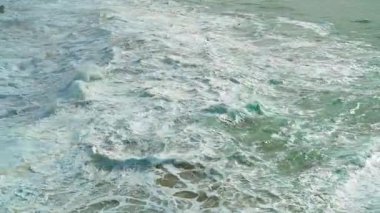 Beyaz köpüklü ve turkuaz renkli güçlü okyanus dalgaları büyüleyici bir şekilde çarpışıp dönüyor. Suyun hareketi dinamik ve enerjik bir atmosfer yaratır. Doğanın gücü kavramı