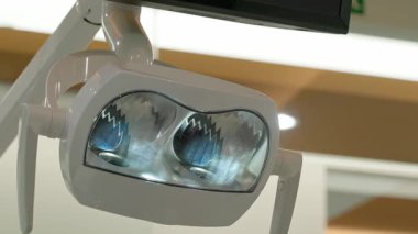 Modern klinikteki ayarlanabilir kollara yansıtıcı lensler takılmış parlak diş cerrahisi lambaları ve beyaz duvarlar.