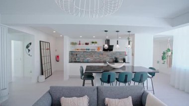 Modern bir açık konsept mutfak ve yaşam alanı parlak siyah bir ada, deniz mavisi bar tabureleri, kolye aydınlatma, dekoratif raflar, ve parlak bir alanda süslü bir döşeme.