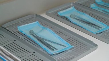 Sterilize edilmiş diş aletleri modern diş hekimliğinde hijyen ve güvenliği sağlamak için temiz ve düzenli klinik ortamda delikli metal tepsilerin üzerine yerleştirilmiş mavi tıbbi çantalara kapatılmıştır.