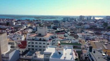 Faro, Portekiz 'in yüksek açılı hava manzarası, şehrin tarihi mimarisi, kırmızı kiremitli çatıları, modern binalar ve botlarla dolu manzaralı Ria Formosa lagünü.