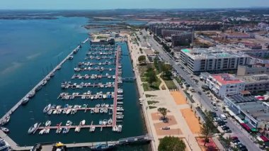 Portekiz, Olhao 'nun çarpıcı insansız hava aracı görüntüsü, açık mavi gökyüzünün altında tekne, rıhtım güvertesi ve geniş Ria Formosa lagünüyle dolu marinayı gösteriyor..