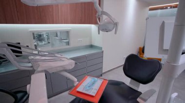 Siyah yastıklı modern dişçi koltuğu, tepe lambası, enstrüman tepsisi, sterilize aletler, tıbbi ekipman ve ahşap dolaplı temiz organize diş kliniğinde ergonomik tasarım.