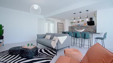 Gri bir kanepe, dekoratif yastıklar ve siyah bir adası, bar taburesi ve kolyesi olan çağdaş bir mutfakla tamamlanmış zebra halısı olan lüks bir yaşam alanı..