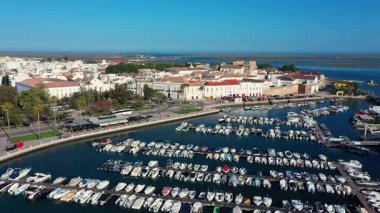 Portekiz 'in Faro şehrinin havadan görünüşü, kayıklarla dolu bir marina, bir rıhtım gezisi, tarihi mimari, ve berrak bir gökyüzünün altındaki Ria Formosa gölünün çarpıcı mavi suları..