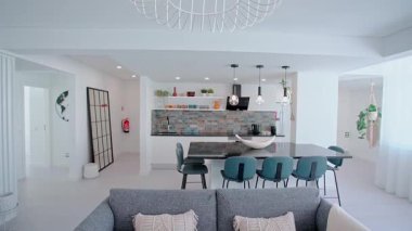 Şık bir açık-plan mutfak ve yaşam alanı parlak bir dekor içinde parlak bir dekorasyon, deniz mavisi bar tabureleri, kolye ışıklandırması, döşeme arkaplanı ve çağdaş bir dekora sahip parlak bir siyah yemek adası içerir..