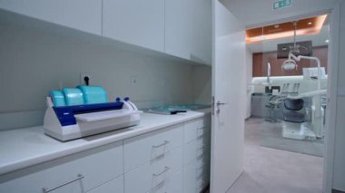 Sterilizasyon odası olan modern bir dişçi kliniği. Tıbbi ekipmanlar ve parlak, temiz bir tedavi alanı. Diş sandalyesi, tepe lambası ve modern mobilyalar..