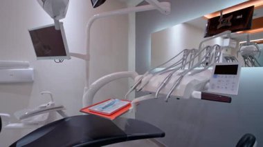El aletleri, hava pulu, dokunmatik ekran kontrol paneli, tepedeki monitör ve modern klinikte parlak ışıklandırma ve temiz ortama sahip ergonomik sandalye gibi diş aletlerinin yakın çekimleri.