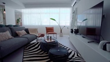 Gri kanepesi, dekoratif yastıkları, siyah kahve masası, zebra desenli halısı, kahverengi deri koltuğu ve rafları olan beyaz bir eğlence merkezi olan modern bir oturma odası..