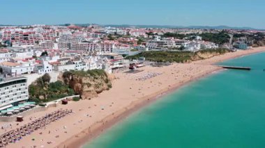 Turkuaz okyanusa bakan beyaz binalar Portekiz 'deki Albufeira plajında dinlenen turistler ve uzaktan görülebilen bir dalgakıran. Hava manzaralı praia dos pescadores.
