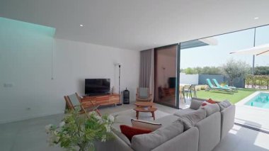 Modern oturma odası doğal ışıkla yıkanmış, zarif havuz ve veranda manzaralı geniş iç mekan, çağdaş tasarım ve minimalist dekor unsurları barındırıyor.