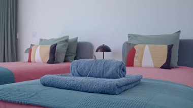 Yumuşak mavi havlular titizlikle sarılmış ve düzenli bir şekilde koordine edilmiş pembe ve deniz mavisi battaniyeler, çağdaş otel odası hazırlığı ve konukseverlik tasarımı sergilenmektedir.