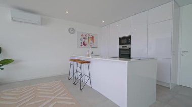 El değmemiş beyaz mutfak gösterişli bir ada, ahşap tabure ve minimalist tasarım elementlerini yavaş yavaş rafine edilmiş mimari odak noktasında ortaya çıkarıyor.