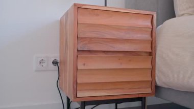 Zarif lamba ve entegre telefon şarj aleti içeren minimalist ahşap komodin. Zarif işlevselliğe sahip çağdaş yatak odası iç tasarımı tamamlayıcı.