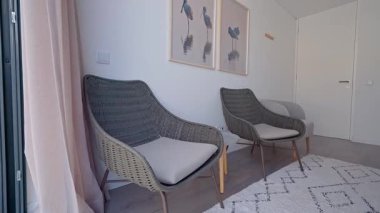 Yastıklı rahat hasır koltuklar, çerçevelenmiş kuş resimleri ve desenli bir halı ile tamamlanmış çağdaş bir oturma odasında rahat bir atmosfer yaratır.