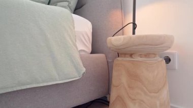 Sıcak ışık modern yatak odasını zarif ahşap komodiniyle aydınlatıyor. İç dizayn detaylarını gösteriyor. Rahat yatak, yumuşak yastıklar ve uygun duvar anahtarı gibi.