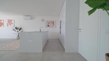 Minimalist beyaz mutfak, bir ada, entegre cihazlar ve sanatsal ayrıntılar içeren modern tasarımı sergiliyor, temiz ve şık bir mutfak alanı yaratıyor.