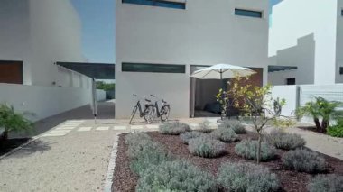 Parlak güneş ışığı, el değmemiş beyaz villa, lavanta bahçesi, teras koltukları, sakin arka bahçe manzarasında park edilmiş bisikletler.
