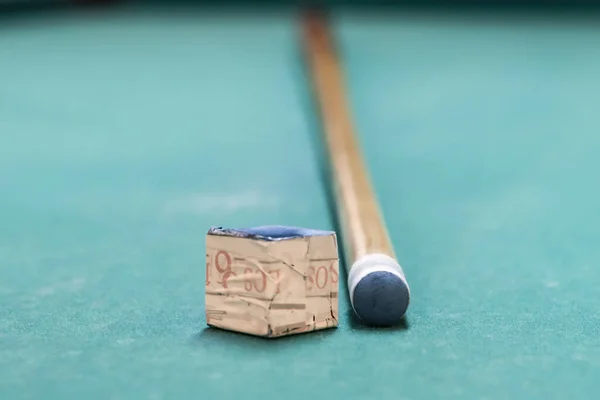 A cue stick and a chalk on a pool table
