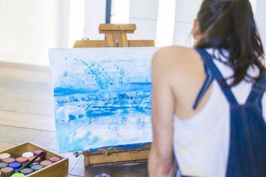 Bir kadın ressam tuvale mavi bir soyut resim çiziyor. Sanat stüdyosunda yerde çalışan yaratıcı bir kadın..