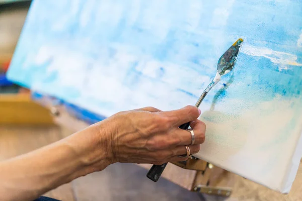 stock image Close up of a woman's hand painting on a canvas a blue abstract painting.