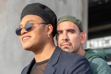 Eşcinsel çift dışarıda yan yana dururken birbirlerine sarılıyorlar. Bir tanesi kameraya bakıyor.